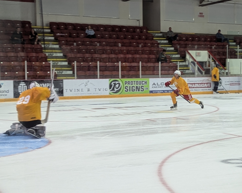 A hockey played in a yellow jersey and red pants shooting at a goaltender in a yellow jersey