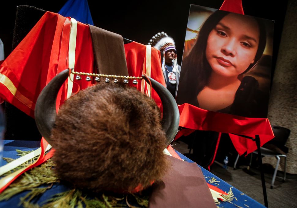 A buffalo cap with fur and horns sits on a table, with a large portrait of an Indigenous woman displayed on an easle in the background