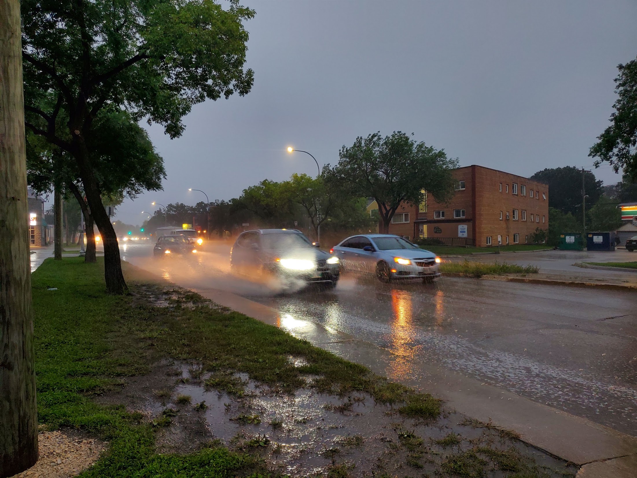 Water splashes out from under a car as morning rush hour traffic drives down a street during a thunderstorm