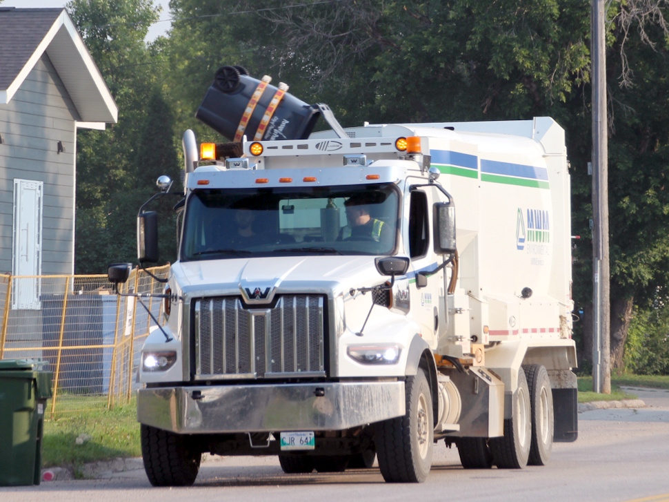 Garbage truck using mechanical arm to lift a black automated garbage cart on a sunny Friday morning in Portage la Prairie.