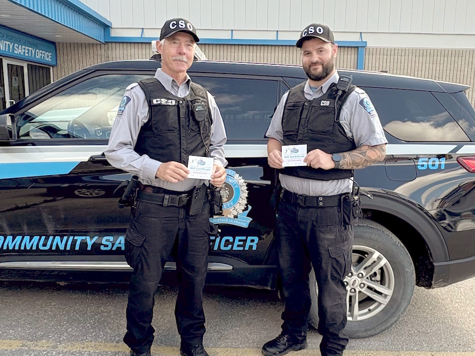 Two Community Safety officers stand next to their safety vehicle, each holding ice cream vouchers, smiling at the camera.