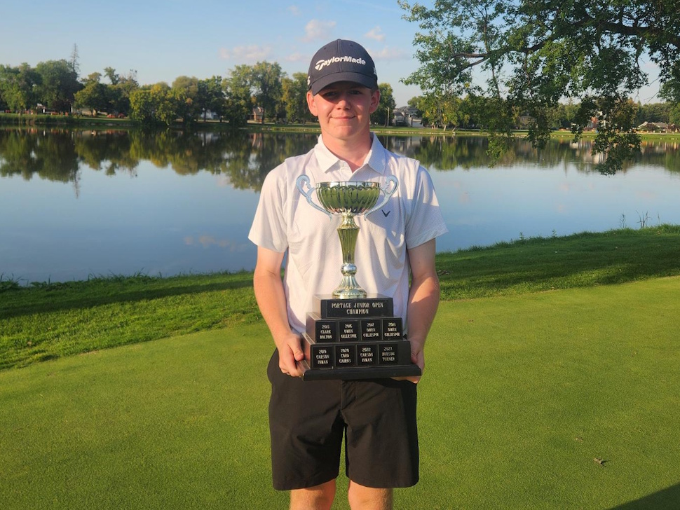 Sixteen-year-old golfer Logan Cairns holds his Stride Credit Union Junior Open trophy on the green at Portage Golf Club with Crescent Lake in the background.