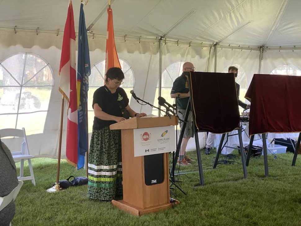 Woman speaking at a podium during the commemorative plaque unveiling ceremony at the Former Portage La Prairie Indian Residential School.