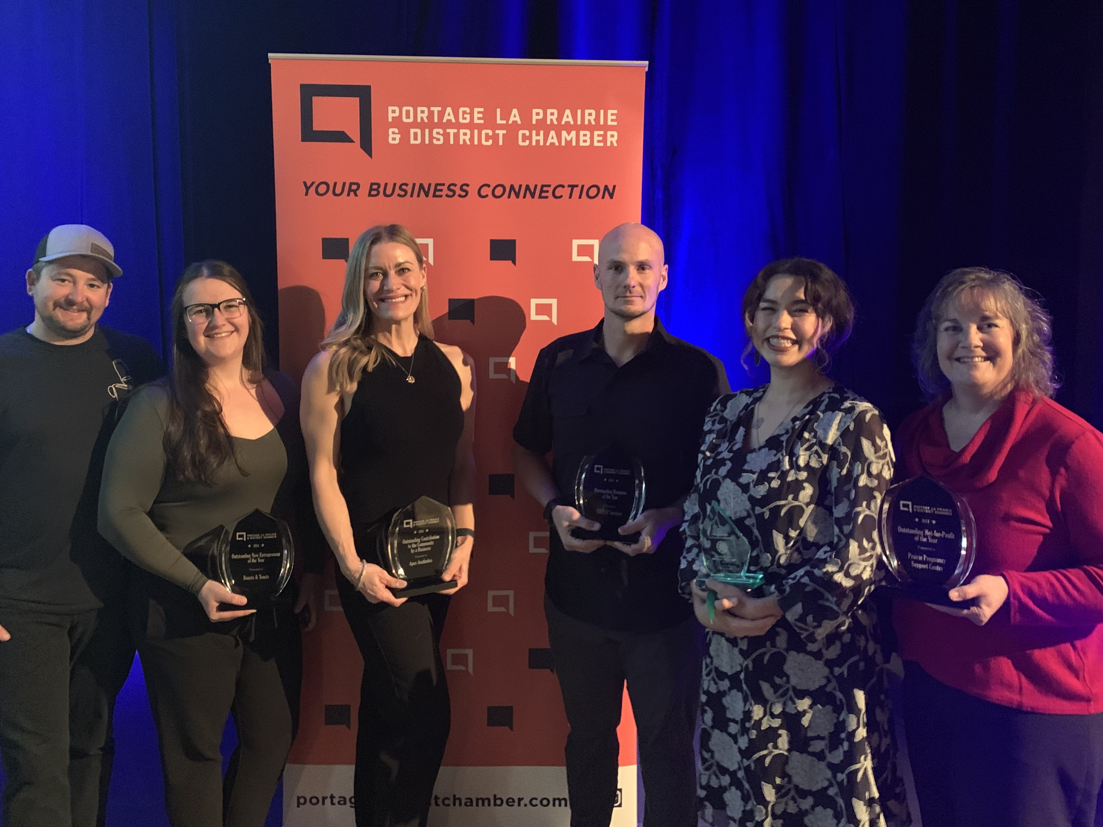 Group photo of previous Best Business Awards winners holding their trophies and smiling at the camera during the awards ceremony.