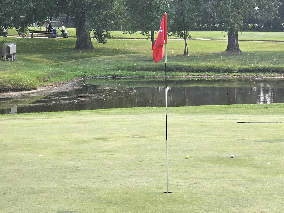 A lush green putting surface at Portage Golf Club under a clear sky, surrounded by trees and manicured fairways.