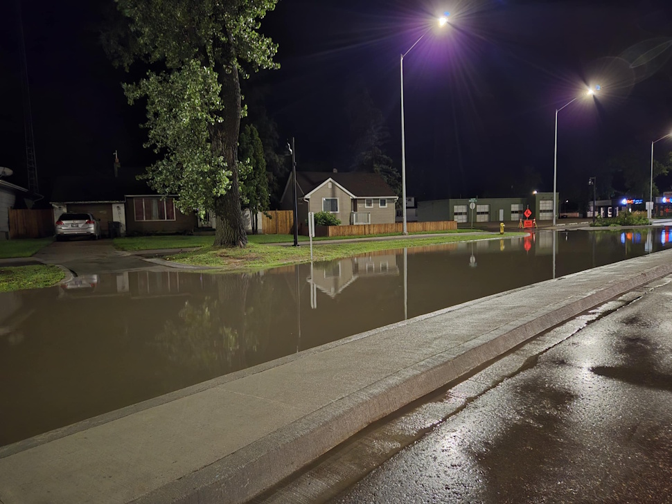 Flooded street on Saskatchewan Avenue West in Portage la Prairie, with water covering the road and partially submerging sidewalks.
