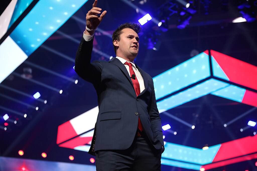 A man points as he speaks on a stage with a colourful background