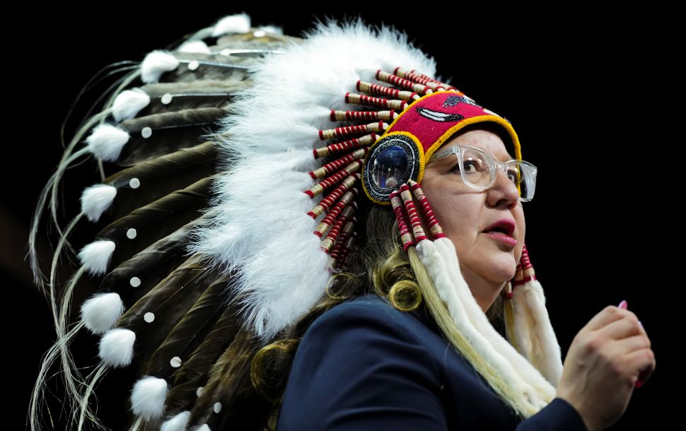A woman wears an Indigenous headdress made with large eagle feathers and colourful beading