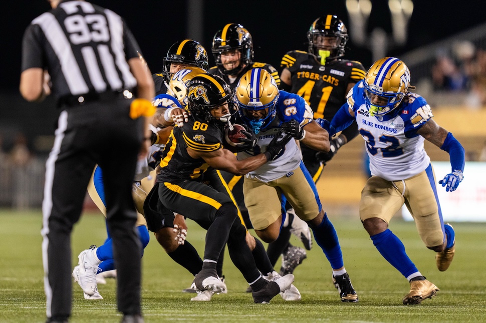 Football players slam together as 1 runs with the ball and others attempt to tackle him