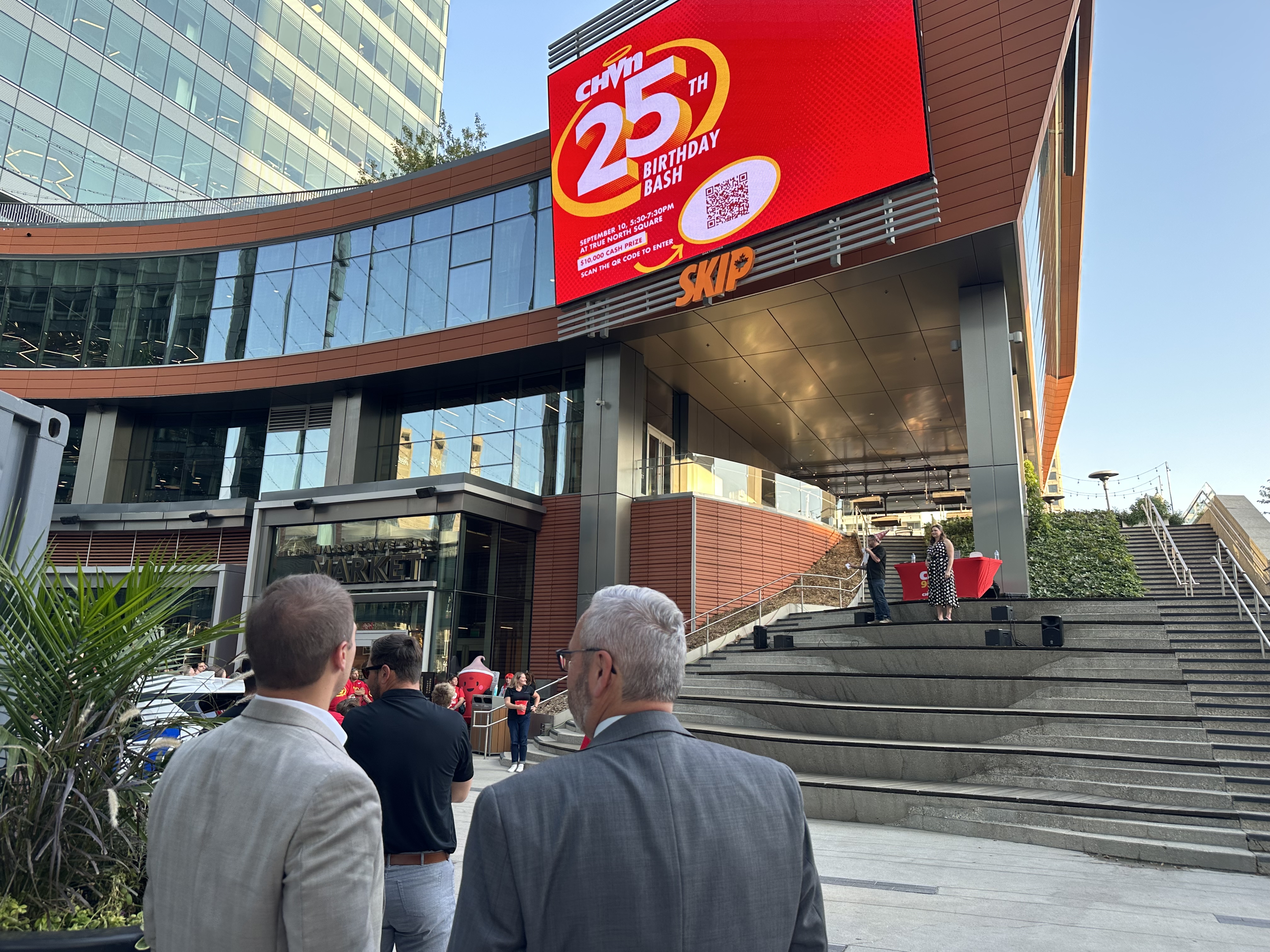 A WIDE ANGLE SHOT SHOWS TRUE NORTH SQUARE AND THE CHVN LOGO ON A LARGE OUTDOOR SCREEN