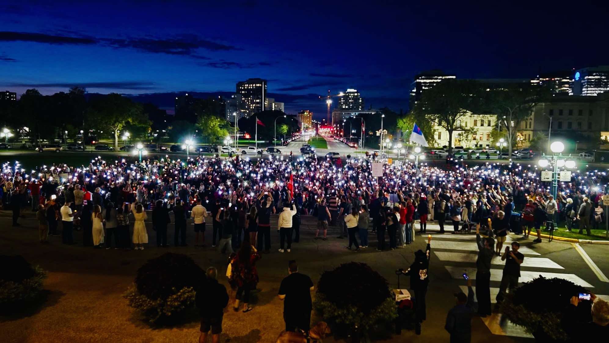 A large crowd at night is lit by candles and cell phone lights 