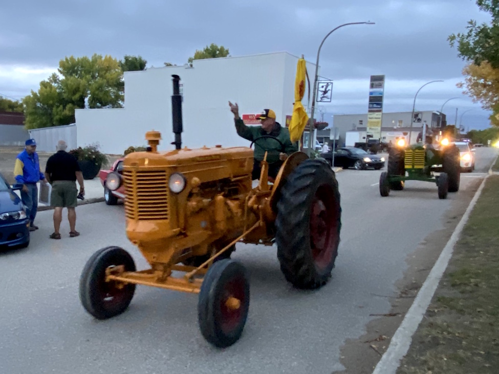 a man sitting on a tractor waves at the people on the side of the road