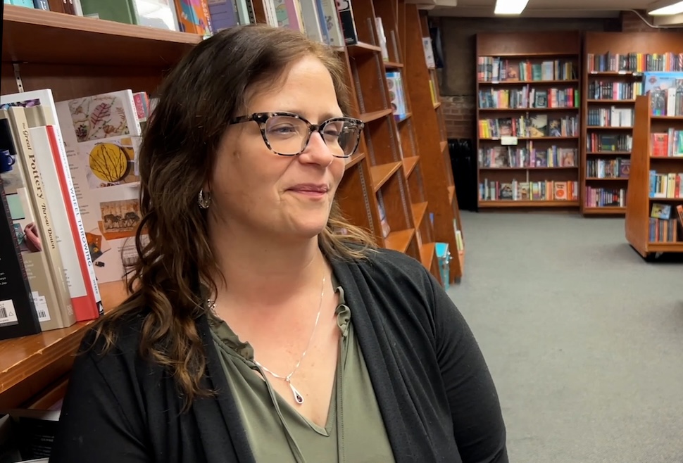 A woman stands in front of a shelf with books inside a bookstore