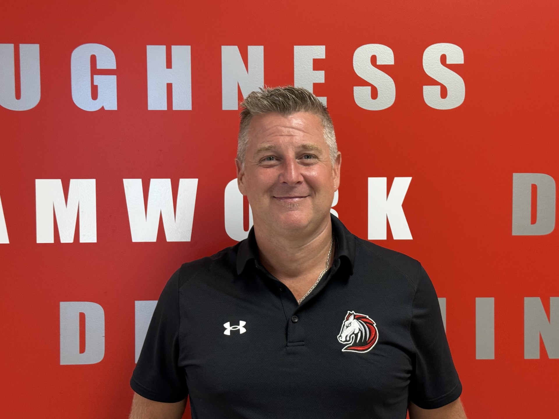 Kyle McKinstry, Principal of MacGregor Collegiate Institute in front of their motto wall