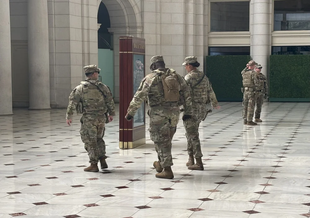 5 people dressed in military fatigues are seen walking and talking in a train station