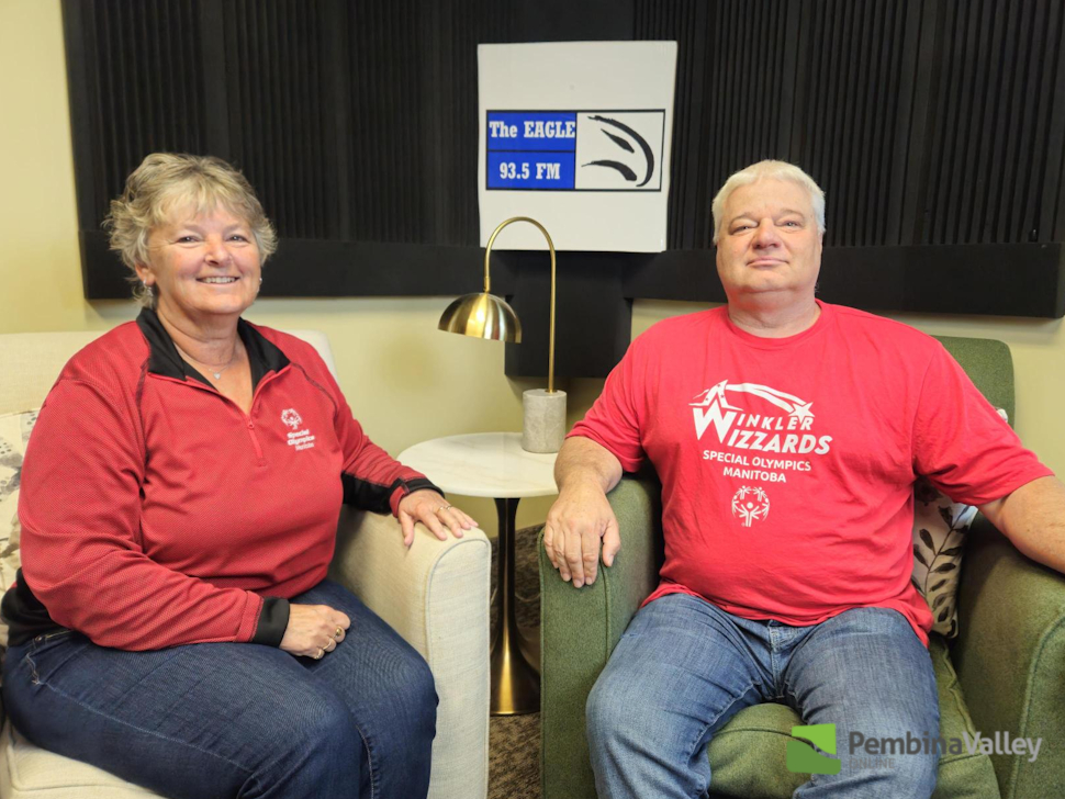 two special olympic coaches in red shirts sit in chairs at the radio station. 