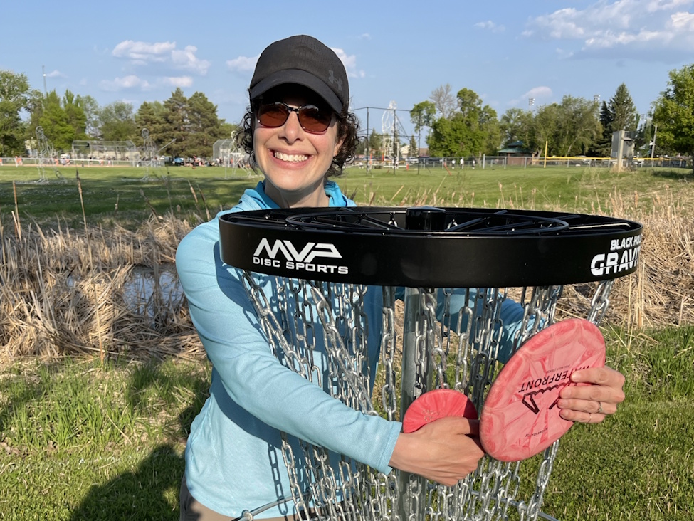a woman smiling while holding a frisbee and a large basket in the summer time