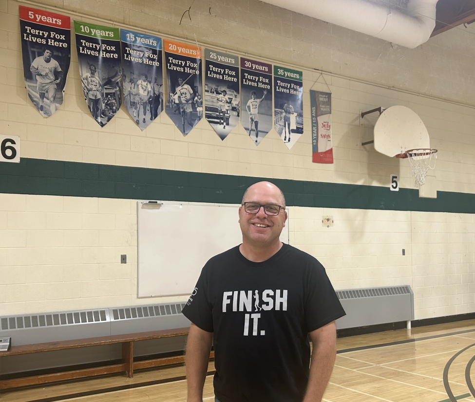 a man standing in a gym with terry fox banners hanging on the wall behind