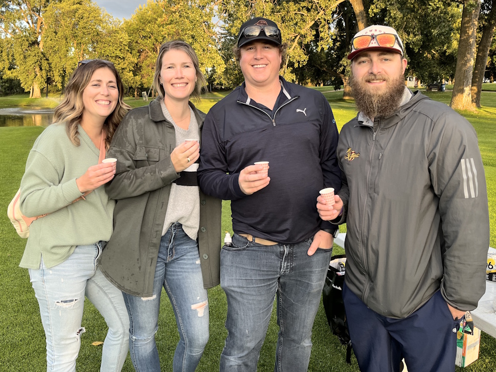Four Sip and Stroll participants walk across the Portage Golf Club course, carrying tasting glasses and enjoying the evening.