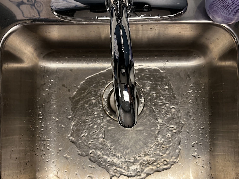 A close-up of a kitchen faucet with water flowing into a stainless steel sink.