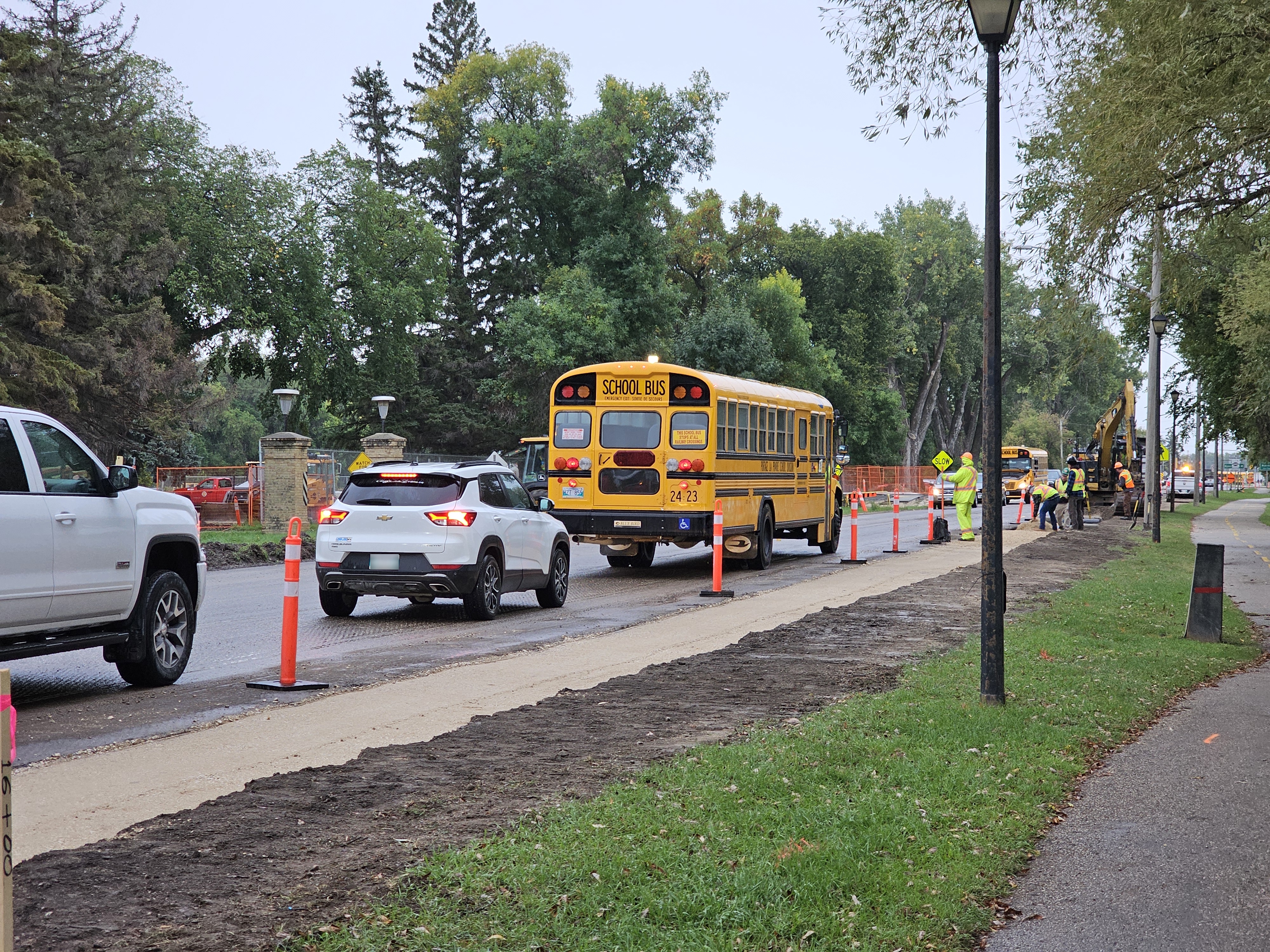 A school bus and vehicles are stopped at a handheld stop sign, waiting for vehicles 500 meters away to pass by before they're allowed to progress.