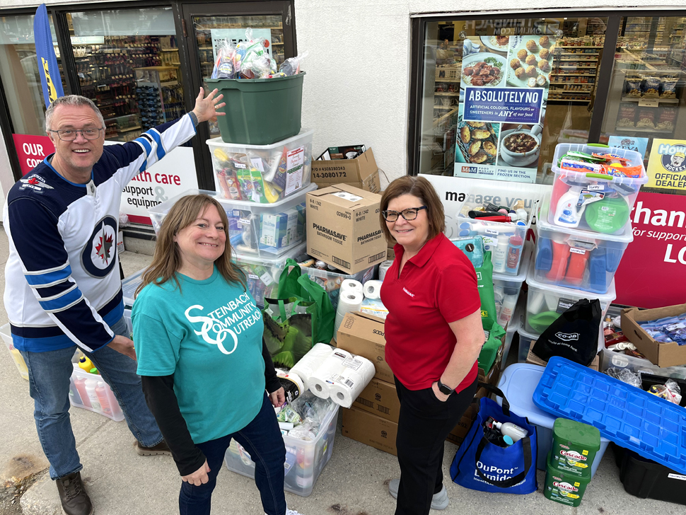 two women and one man stand in front of a mount of boxes filled with soap