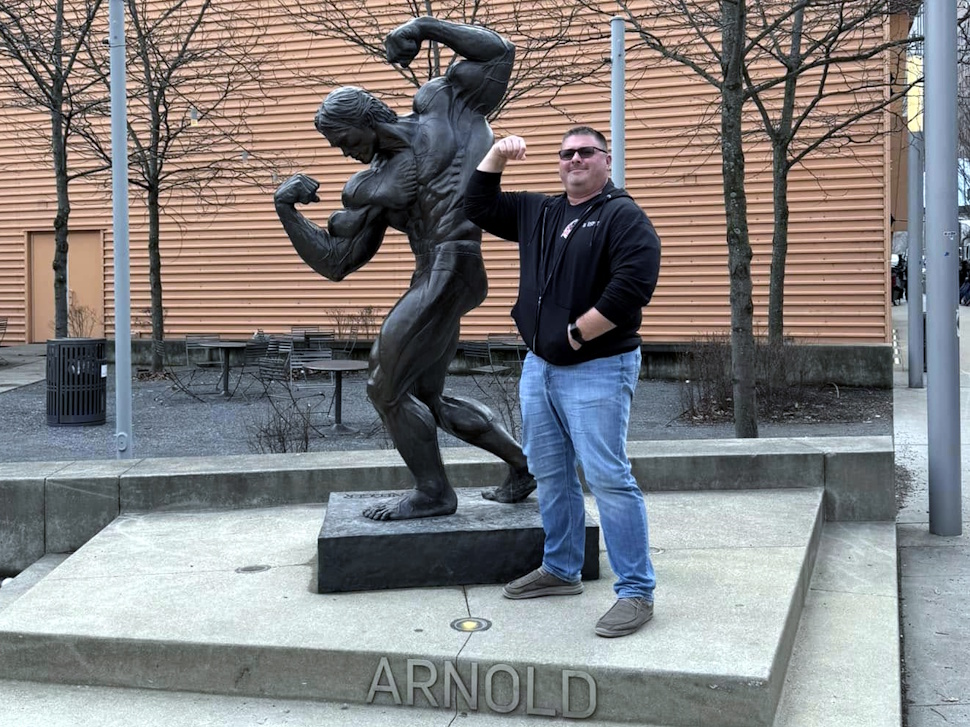 Ryan Espey stands next to a bronze statue of Arnold Schwarzenegger in Columbus, Ohio.