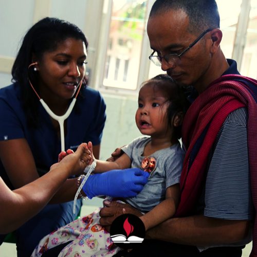 A man holds a baby while a doctor does a check-up on the child