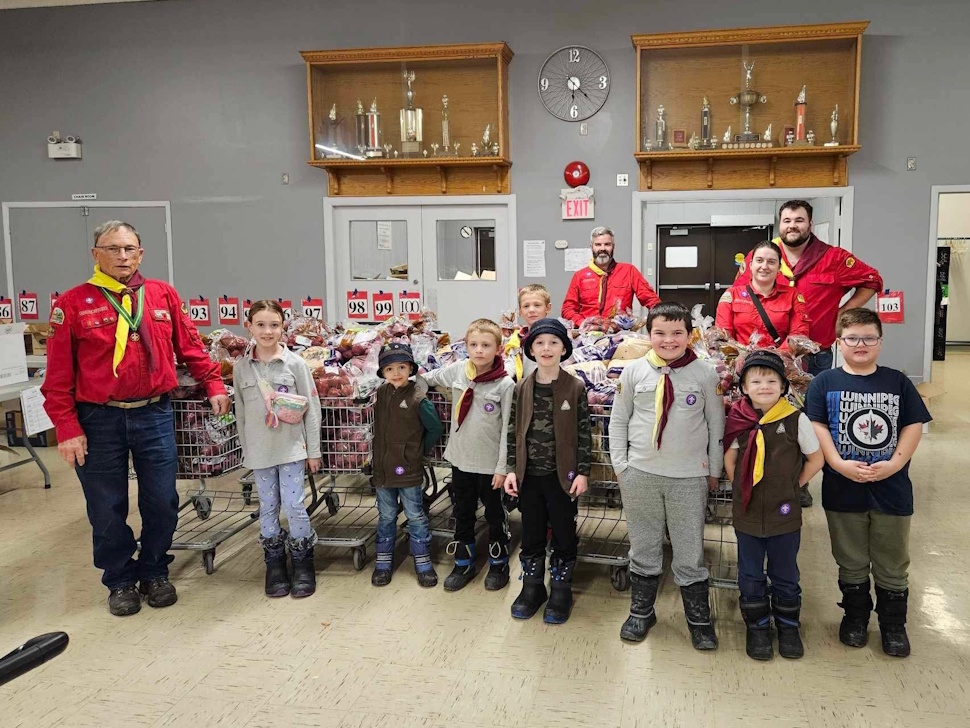 A group of young Scouts and volunteers carrying boxes of food into a community donation center.