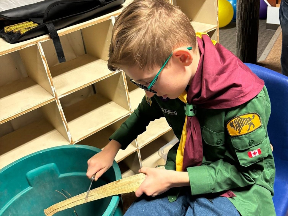 A young participant practices woodworking skills during a carving activity, part of the group’s hands-on learning and outdoor programs. Facebook/Carman Beavers, Cubs & Scouts