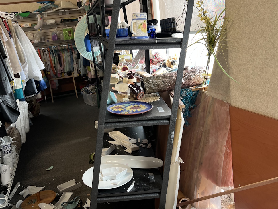 Interior view of GME Thrift Emporium showing the south wall pushed inward with visible cracks and debris scattered around.