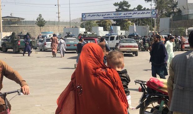 A woman holds a child in the middle of a crowd in front of an airport entrance