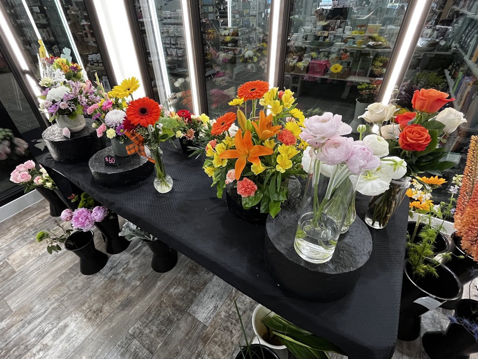 Shelves filled with colorful fresh flowers inside the walk-in cooler at Mil-Jeanne Flowers & Axcenz, including roses, lilies, and gerbera daisies.