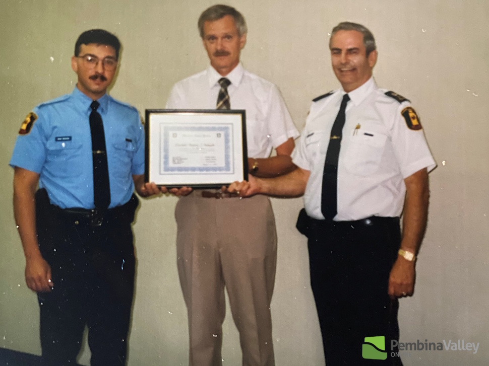 three people stand in a row with a framed document