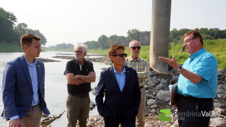 A group of men stand on the shores of a very low river with rocks in the background