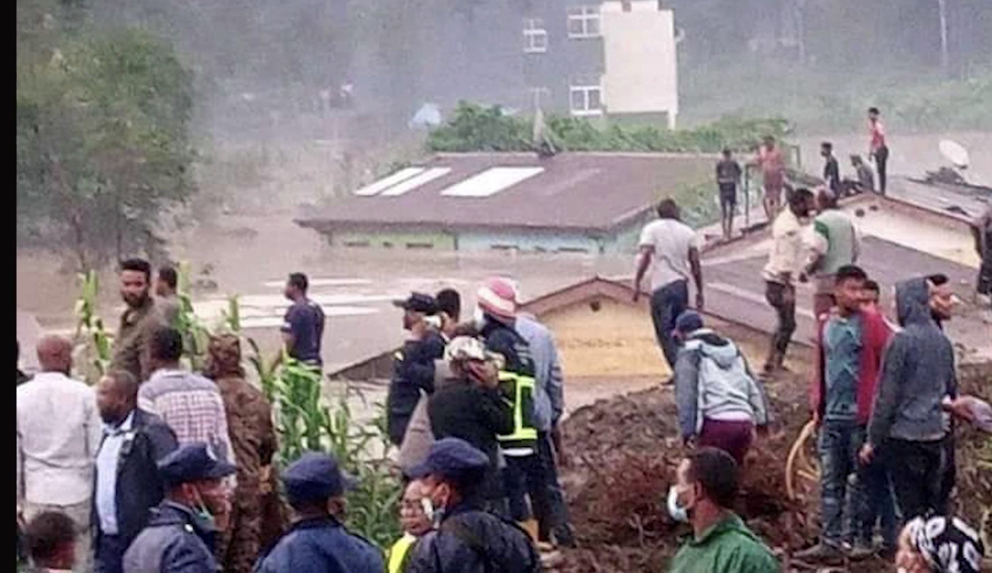 People stand on the roof of a building. Water is up to the bottom of the roof.