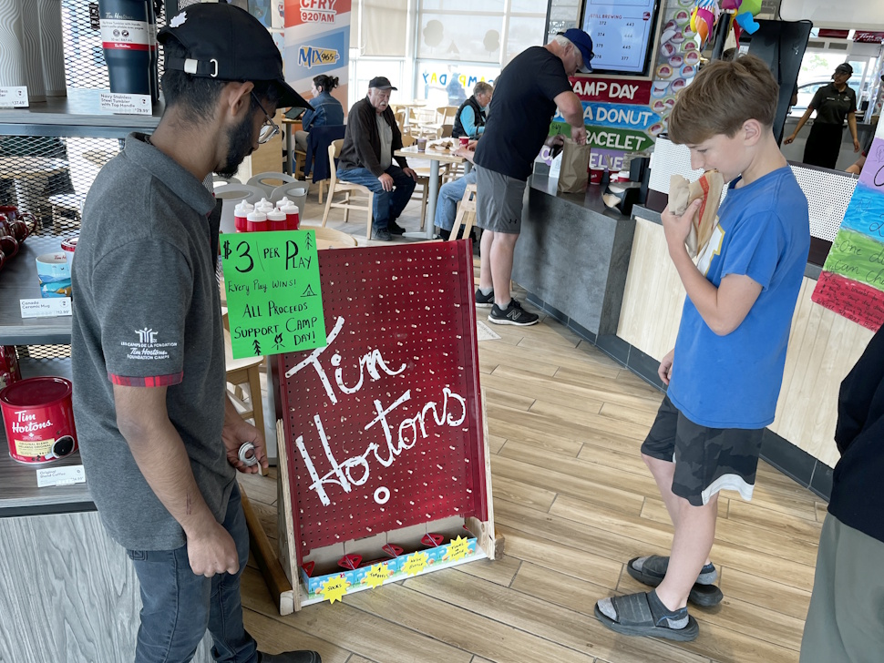 A young child plays a game of Plinko at the West End Tim Hortons, aiming to win a prize by dropping a chip down the board.