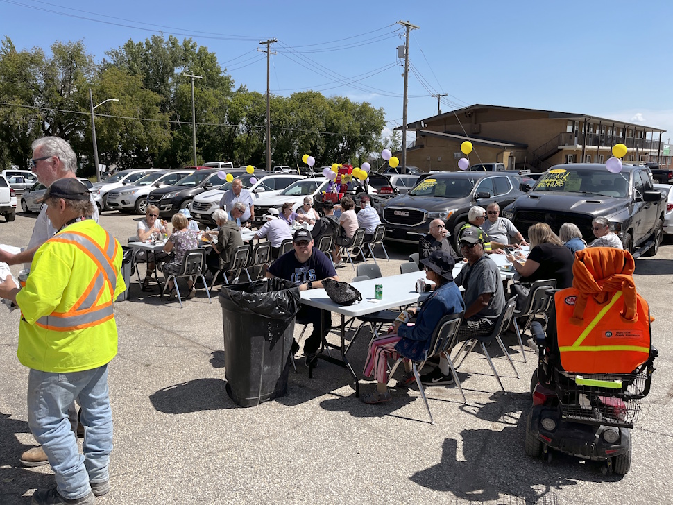Crowd of people sitting at tables, eating and socializing at an outdoor fundraiser barbecue.