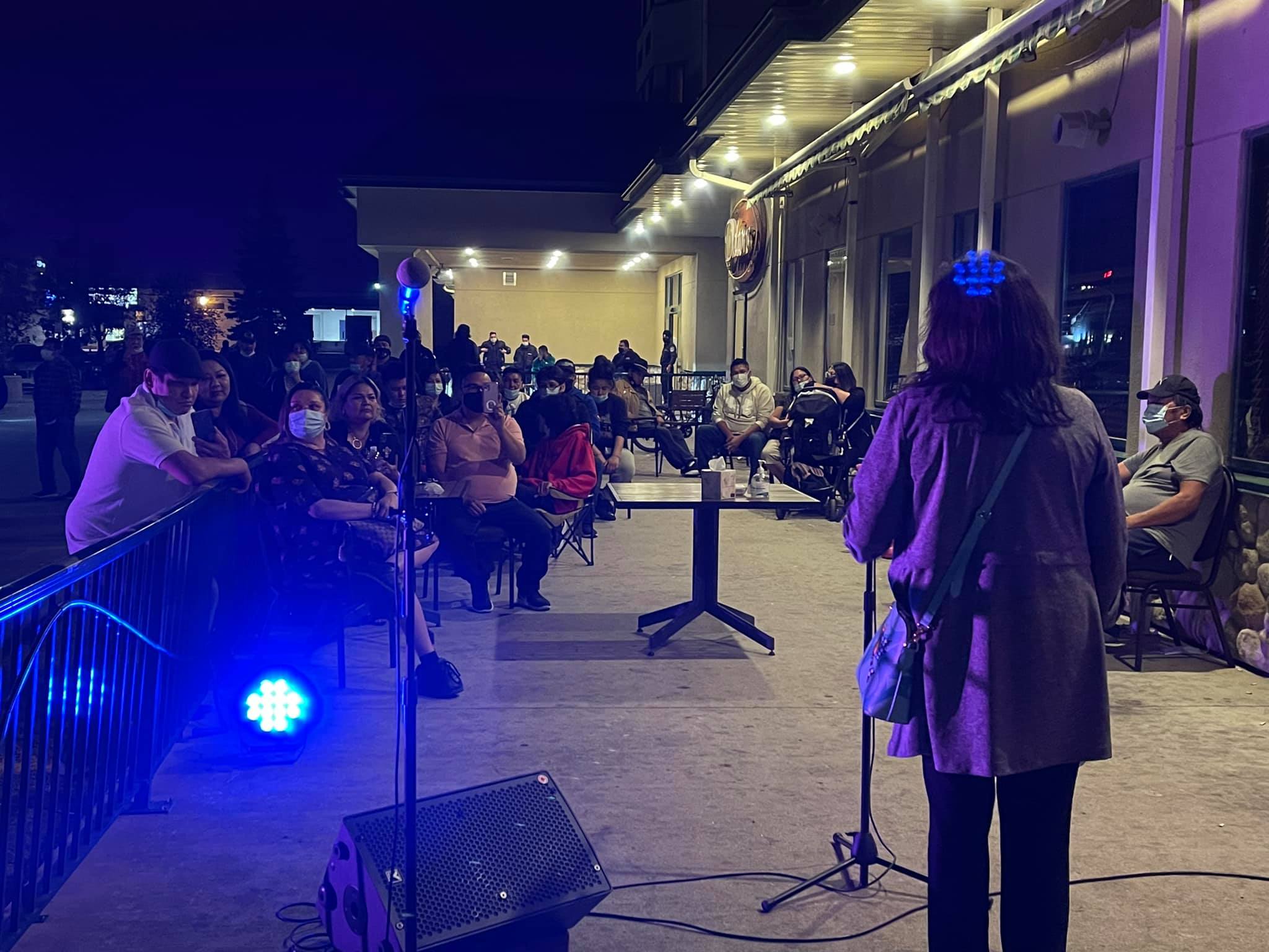 A woman speaks to a crowd of people on the front sidewalk of the hotel