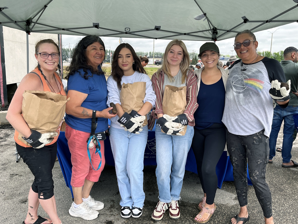 Organizers and summer students smile while holding potatoes during a group photo at the produce giveaway.