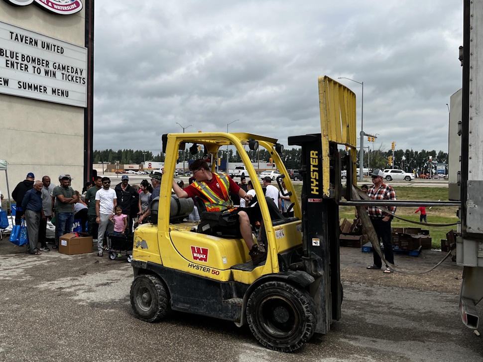 A forklift moves a pallet of produce off a delivery truck during a community food giveaway.