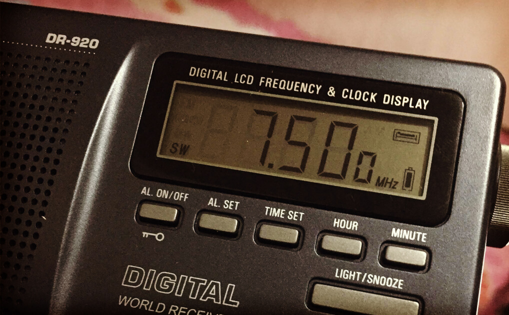 a closeup of a digital radio. a LCD display shows the radio tuned to 7.50 MHz. A number of buttons for setting time, etc. are below the frequency