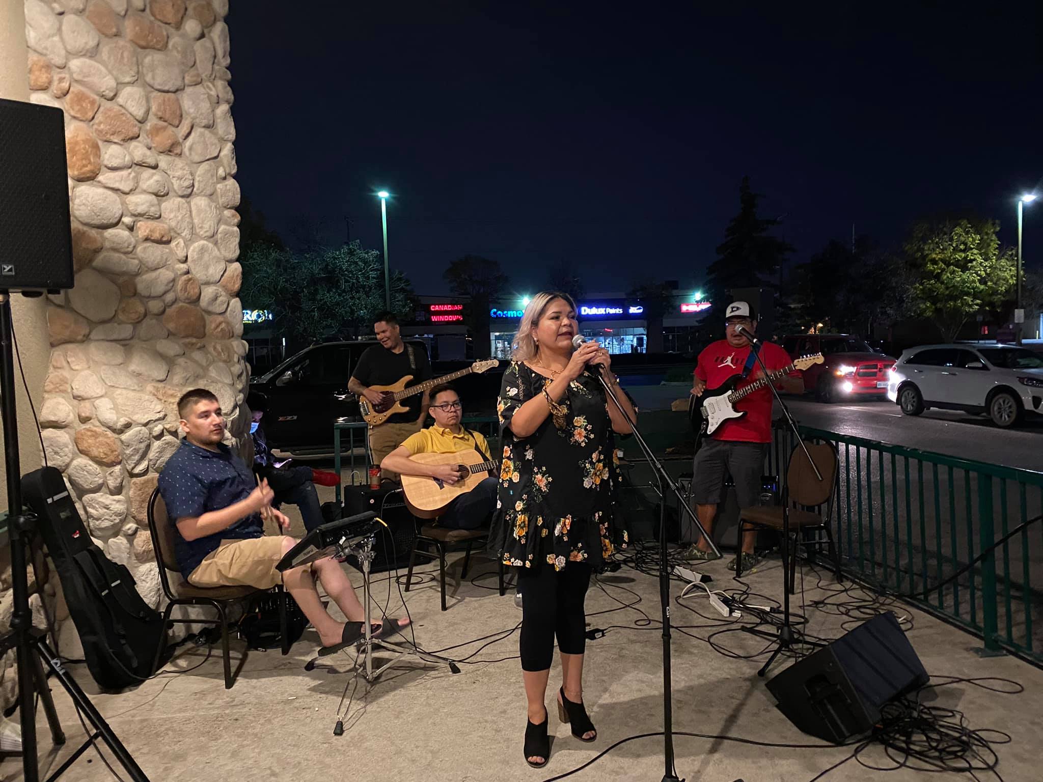 A woman sings behind a microphone with a group of men playing guitars behind her.