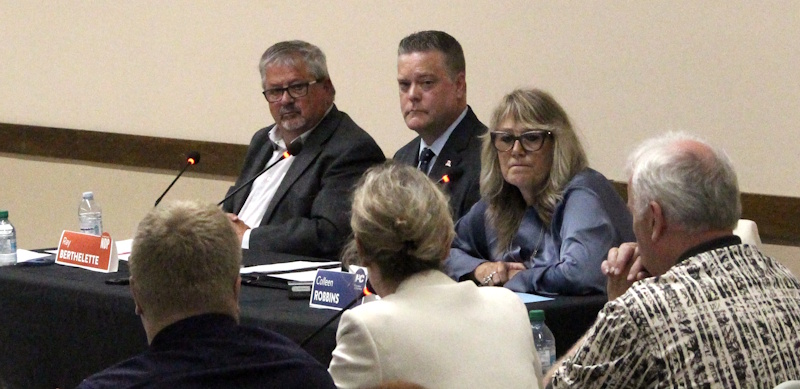 three people listening to a panel during a political debate