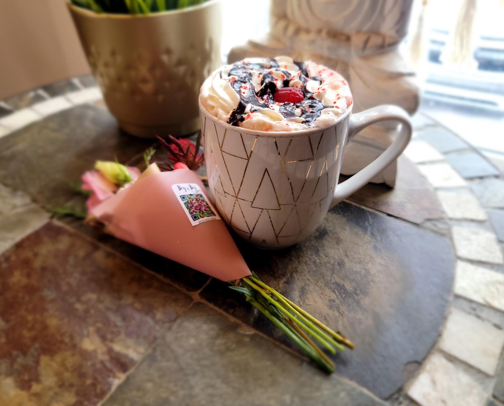 A cup of hot chocolate next to a miniature bouquet of flowers.
