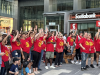 2 DOZEN PEOPLE IN RED SHIRTS RAISE THEIR HANDS